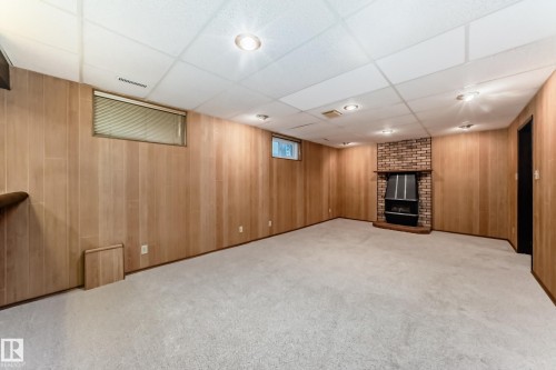 Spacious room featuring light wood-panel walls, plush carpeting, and a brick-faced fireplace with an insert - 12022 62 Street, Edmonton, AB 