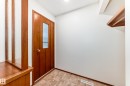 Entryway featuring a wood-panel door with a frosted glass insert, neutral tiled flooring, a built-in wood partition with integrated shelving, and a recessed ceiling light - 12022 62 Street, Edmonton, AB 