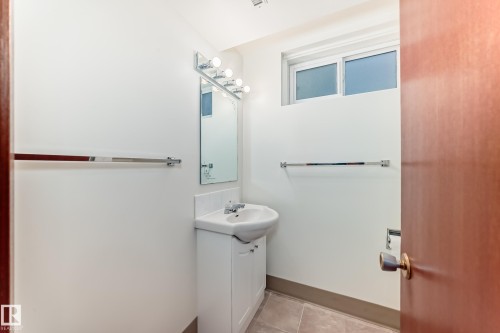 Bathroom featuring a white pedestal sink with integrated storage, a wall-mounted mirror, and a chrome light fixture - 12022 62 Street, Edmonton, AB 