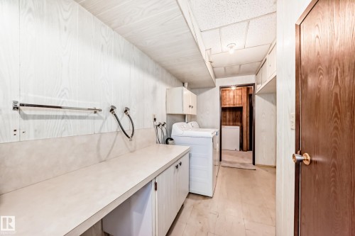 Utility room featuring expansive counter space with an integrated sink, white wood-finish wall paneling, and a drop ceiling - 12022 62 Street, Edmonton, AB 