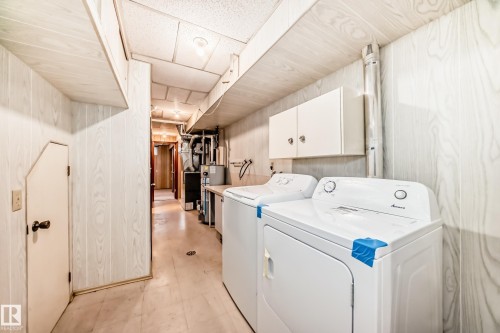 Dedicated laundry area featuring a white washer and dryer set, overhead white cabinetry, and light wood-finish paneling - 12022 62 Street, Edmonton, AB 