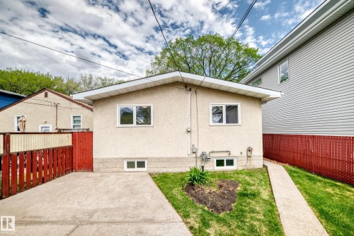 Rear exterior featuring stucco finish, white-framed windows, a concrete driveway, and a red wooden fence - 12022 62 Street, Edmonton, AB 