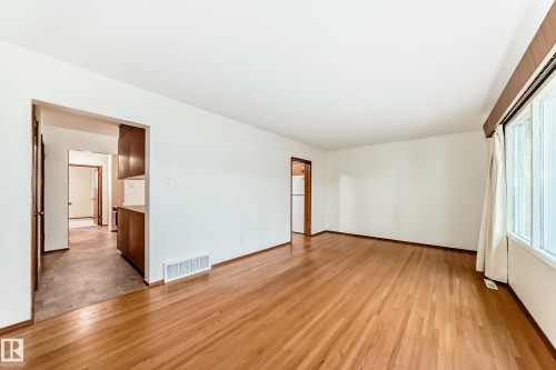 Spacious room featuring wood-finish flooring, white walls, and a large window with vertical blinds - 12022 62 Street, Edmonton, AB 
