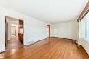Spacious room featuring wood-finish flooring, white walls, and a large window with vertical blinds - 12022 62 Street, Edmonton, AB 