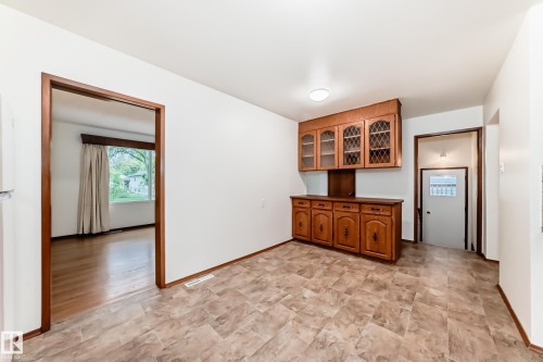 Interior space featuring built-in wood cabinetry with glass-front uppers and solid lower cabinets, light-toned vinyl flooring, and white walls - 12022 62 Street, Edmonton, AB 
