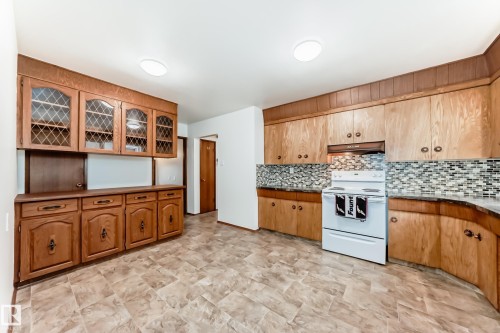 Kitchen featuring wood-finish cabinetry, patterned backsplash, a built-in oven, and durable flooring - 12022 62 Street, Edmonton, AB 