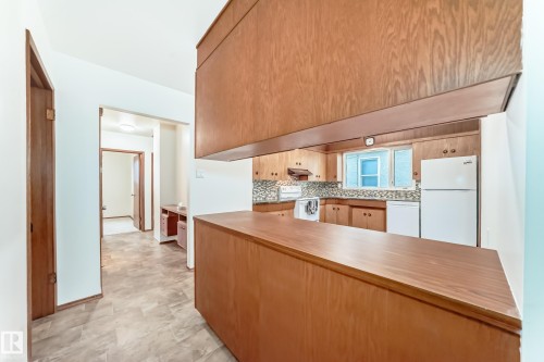 Kitchen with wood-finish cabinetry, white appliances, and a pass-through counter - 12022 62 Street, Edmonton, AB 