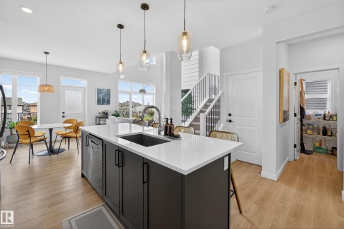 Bright open-concept kitchen featuring a large island with sink, pendant lighting, wood-finish flooring, and ample natural light from multiple windows - 17023 45 Street, Edmonton, AB 