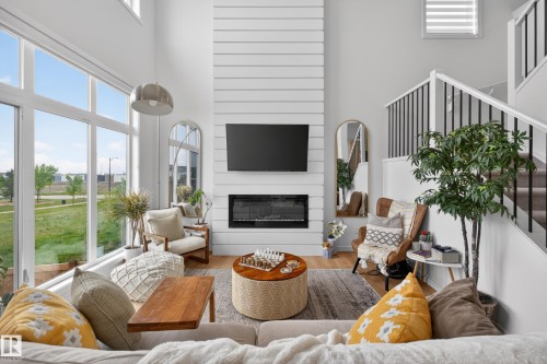 Two-story living area featuring a shiplap fireplace surround, floor-to-ceiling windows, and a staircase with open black spindles - 17023 45 Street, Edmonton, AB 