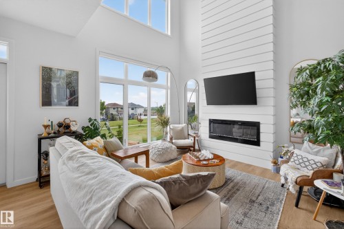 Living area featuring a floor-to-ceiling shiplap fireplace with an electric insert, wood-finish flooring, and expansive windows - 17023 45 Street, Edmonton, AB 
