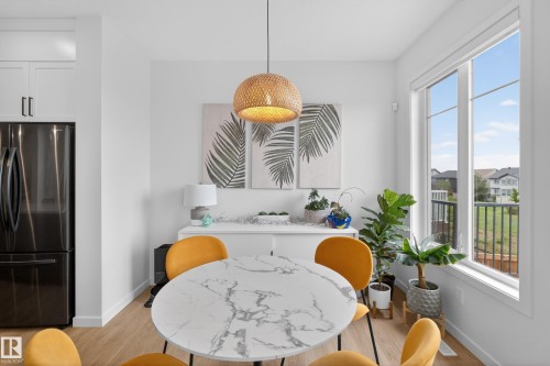 Dining area featuring a circular white-veined stone-finish table, wood-finish flooring, a contemporary woven pendant light, and a large window - 17023 45 Street, Edmonton, AB 