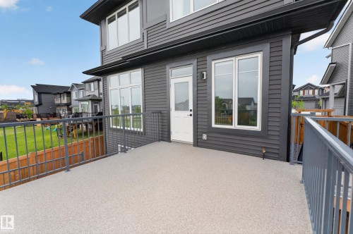 Spacious outdoor deck featuring light-colored resurfacing, a white egress door, and contemporary metal railings - 17023 45 Street, Edmonton, AB 
