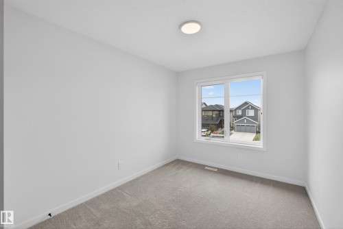 Spacious room featuring neutral carpeting, white baseboards, a large multi-pane window, and a flush-mount ceiling light fixture - 17023 45 Street, Edmonton, AB 