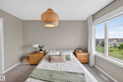 Carpeted bedroom featuring a large window, a woven pendant light fixture, and light neutral wall colors - 17023 45 Street, Edmonton, AB 