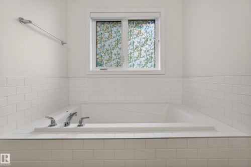 Built-in soaking tub featuring subway tile surround, polished chrome fixtures, and an opaque window with decorative film - 17023 45 Street, Edmonton, AB 