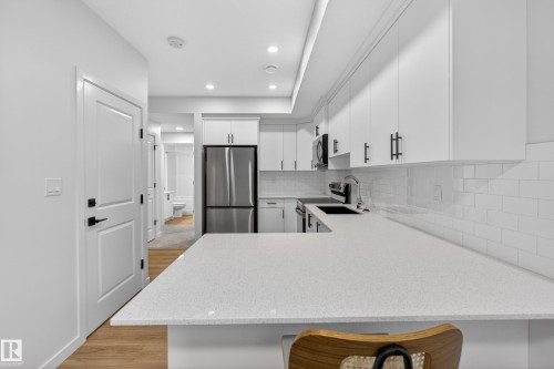 Contemporary kitchen featuring white cabinetry, light-colored countertops, a subway tile backsplash, stainless steel refrigerator, and wood-finish flooring - 17023 45 Street, Edmonton, AB 