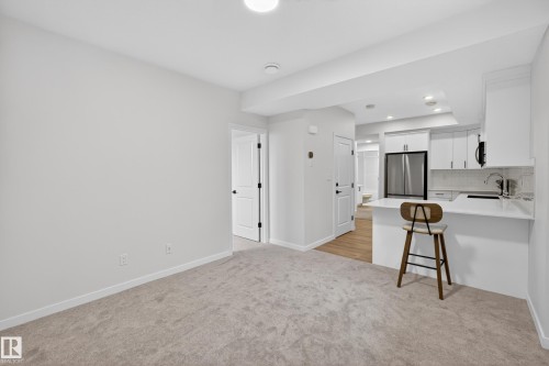 Open-concept kitchen featuring white cabinetry, stainless steel appliances, and a breakfast bar with a white countertop - 17023 45 Street, Edmonton, AB 