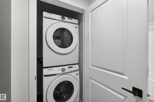 Dedicated laundry closet featuring a stackable washer and dryer, white paneled door with matte black hardware, and an adjacent white bathtub - 17023 45 Street, Edmonton, AB 