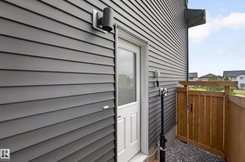 Exterior features include dark gray horizontal siding, a white entry door with privacy glass, a black cylindrical outdoor light fixture, a wooden privacy fence, and a gravel ground cover - 17023 45 Street, Edmonton, AB 