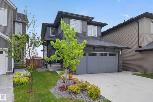 Contemporary two-story residence with a dark gray exterior, featuring a two-car attached garage, concrete driveway, and front landscaping with mature trees and shrubs - 17023 45 Street, Edmonton, AB 