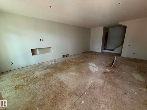 Expansive room featuring a recessed wall niche, light-toned wall finishes, and a visible staircase - 10985 130 Street, Edmonton, AB 