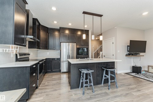 Modern kitchen featuring dark wood-finish cabinetry, stainless steel appliances, a center island with pendant lighting, light-toned countertops, and wood-finish flooring - 8744 223 Street Nw, Edmonton, AB 