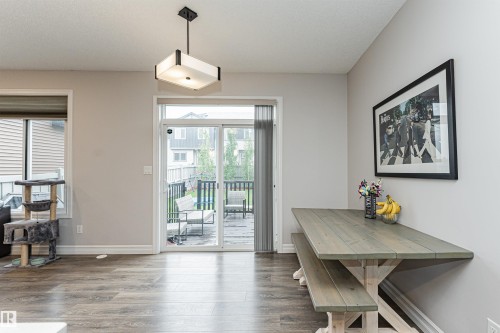 Open-concept interior featuring wood-finish flooring, a contemporary ceiling light fixture, and a sliding glass door leading to a deck - 8744 223 Street Nw, Edmonton, AB 