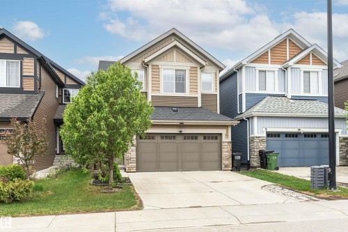 Two-story residence featuring a two-car garage with panel detailing, stone veneer accents, horizontal siding, and a gabled roofline - 8744 223 Street Nw, Edmonton, AB 