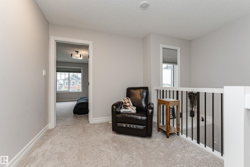 Upper-level landing bonus area, featuring light-toned carpeting, white baseboards, and a contemporary railing with black balusters - 8744 223 Street Nw, Edmonton, AB 
