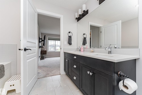 Bathroom featuring a double vanity with a dark wood-finish cabinet, light countertop, and dual sinks with chrome fixtures - 8744 223 Street Nw, Edmonton, AB 