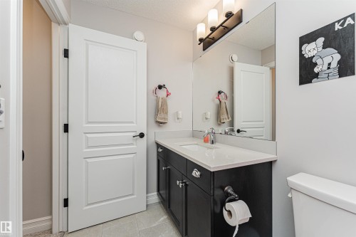 Bathroom featuring a dark wood-finish vanity with a light countertop, an integrated sink with a chrome faucet, a large wall-mounted mirror, and tile flooring - 8744 223 Street Nw, Edmonton, AB 