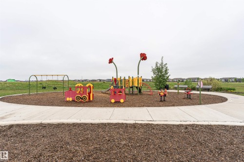 Community playground featuring swings, a train-themed play structure, and spring riders set on a wood chip base - 8744 223 Street Nw, Edmonton, AB 