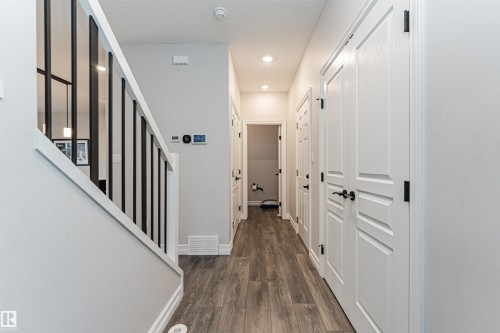 Foyer featuring wood-finish flooring, white paneled doors with black hardware, recessed ceiling lighting, a modern staircase with black balusters, and a light gray wall color - 8744 223 Street Nw, Edmonton, AB 