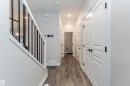 Foyer featuring wood-finish flooring, white paneled doors with black hardware, recessed ceiling lighting, a modern staircase with black balusters, and a light gray wall color - 8744 223 Street Nw, Edmonton, AB 