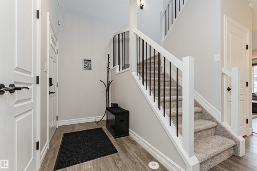Foyer featuring wood-finish flooring, white trim, and a staircase with carpeted treads and black metal spindles - 8744 223 Street Nw, Edmonton, AB 