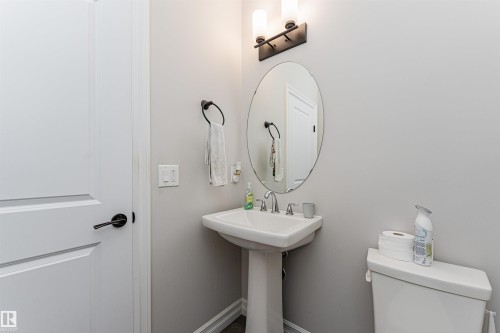 Pedestal sink with chrome faucet, oval mirror, and contemporary two-light vanity fixture - 8744 223 Street Nw, Edmonton, AB 