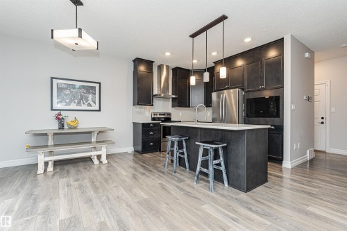 Contemporary kitchen featuring dark wood cabinetry, stainless steel appliances, and a central island with integrated seating - 8744 223 Street Nw, Edmonton, AB 
