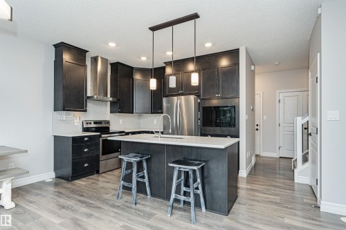 Modern kitchen featuring a central island with integrated sink, pendant lighting, and dark wood-finish cabinetry - 8744 223 Street Nw, Edmonton, AB 