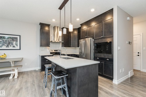 Kitchen featuring dark wood-finish cabinetry, stainless steel appliances, and a central island with white countertop - 8744 223 Street Nw, Edmonton, AB 