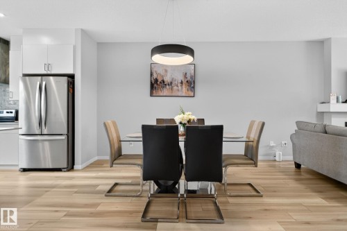 Open-concept dining area featuring light wood-finish flooring, a modern circular pendant light fixture, and light gray wall paint - 1213 16A Street, Edmonton, AB 