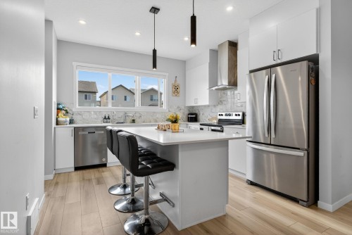 Modern kitchen featuring a central island, white cabinetry, stainless steel appliances, and wood-finish flooring - 1213 16A Street, Edmonton, AB 