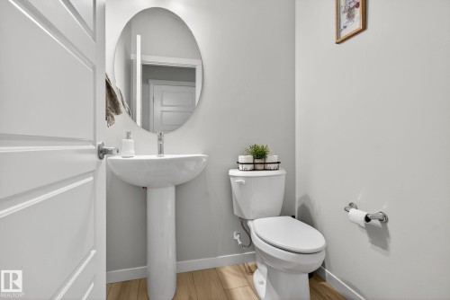 Pedestal sink with chrome faucet, oval mirror, and wood-finish flooring - 1213 16A Street, Edmonton, AB 