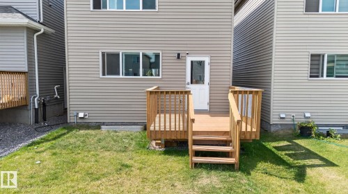 Rear exterior featuring a wooden deck with railing and stairs, a white door, and light-colored horizontal siding - 1213 16A Street, Edmonton, AB 