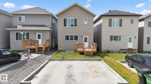 Two-story property featuring light tan vinyl siding, a dark shingle roof, and a rear wooden deck with stairs - 1213 16A Street, Edmonton, AB 