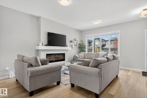 Living area featuring light wood-finish flooring, a contemporary fireplace with a white mantel, recessed ceiling lighting, and large windows with white trim - 1213 16A Street, Edmonton, AB 