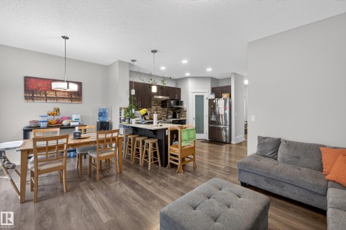 Spacious open-concept living area featuring wood-finish flooring, a kitchen island with seating, dark wood cabinetry, and a stone-tile backsplash - 1404 25 Avenue, Edmonton, AB 