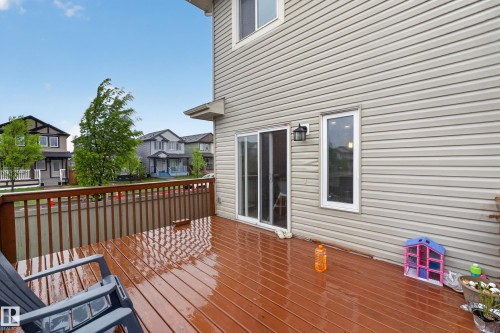 Expansive wood-finish deck with a brown railing, beige horizontal siding, a sliding glass door, and a white-framed window - 1404 25 Avenue, Edmonton, AB 