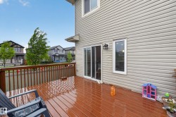 Expansive wood-finish deck with a brown railing, beige horizontal siding, a sliding glass door, and a white-framed window - 