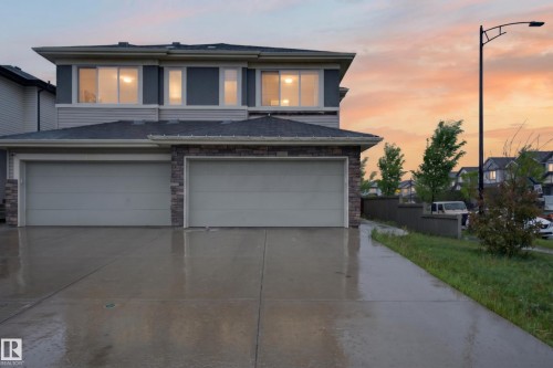 Contemporary residential exterior featuring a two-car garage, stone veneer accents, light gray siding, and a concrete driveway - 1404 25 Avenue, Edmonton, AB 