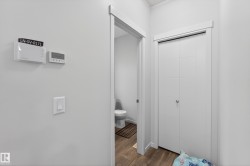 Hallway with white walls, wood-finish flooring, a white light switch, and two wall-mounted thermostats - 